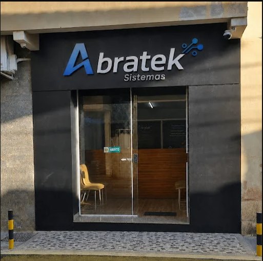 Fachada da loja da Abratek Sistemas, com a placa iluminada e a porta de vidro aberta ao público